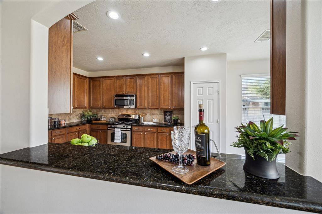 This kitchen features granite countertops, stainless steel appliances, and rich wood cabinetry. The open layout includes a serving bar, perfect for entertaining, with a view into the adjacent room. Natural light brightens the space through the breakfast nook window.