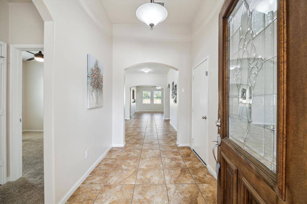 Bright entryway with tiled flooring, arched doorway, and a decorative glass front door, leading to an open living space. Secondary Bedrooms are directly to your left at the front of the home.