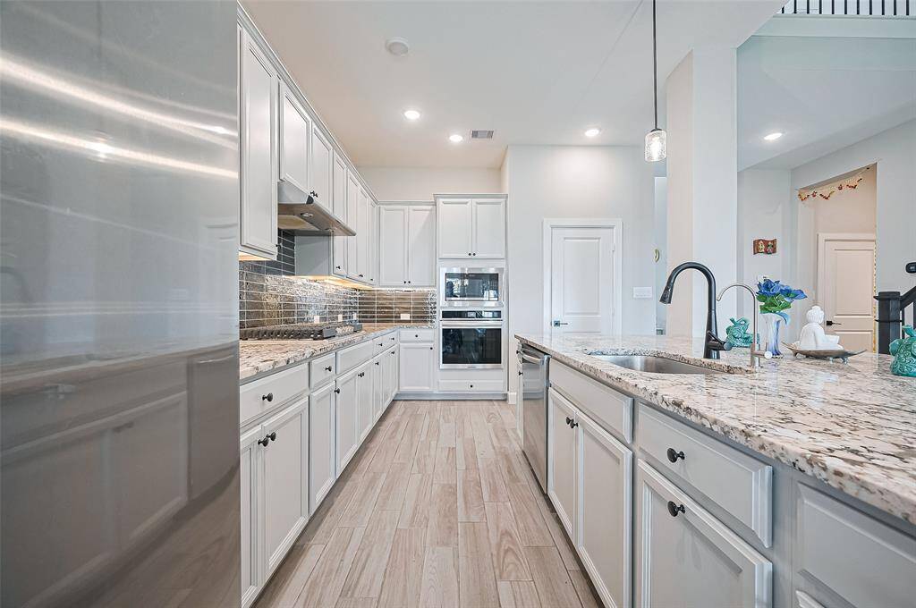 Chef’s dream kitchen features granite countertops, custom backsplash, white cabinetry, a gas cooktop, built-in double ovens, and a walk-in pantry.
