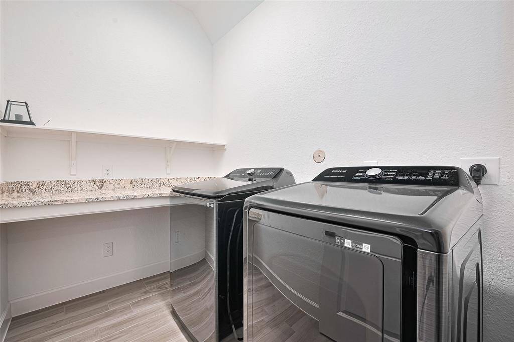 This well-appointed utility room features a modern washer and dryer setup, granite countertop workspace, and upper shelving for convenient storage