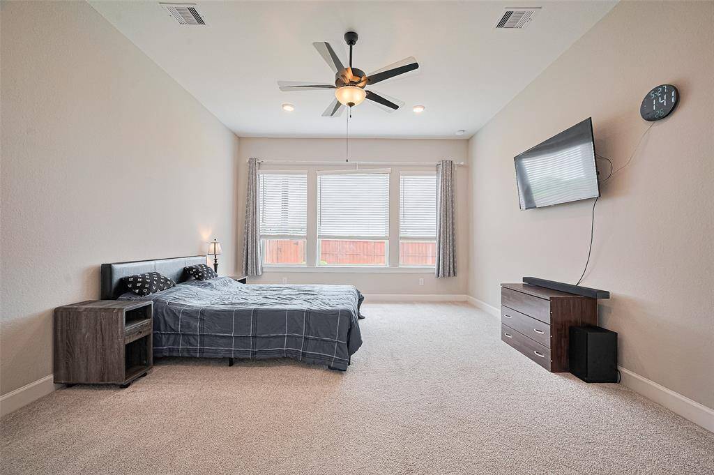 Expansive primary bedroom with a wall of windows, soft carpet flooring, and ceiling fan—offering a private retreat filled with natural light