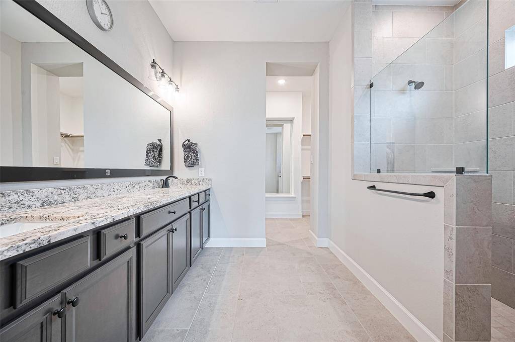 This spa-inspired primary bathroom features a sleek double vanity with granite countertops, framed mirror, and elegant lighting