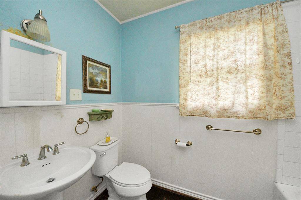 A pop of color brightens this spacious bathroom, featuring a classic pedestal sink and a tub-shower combo.