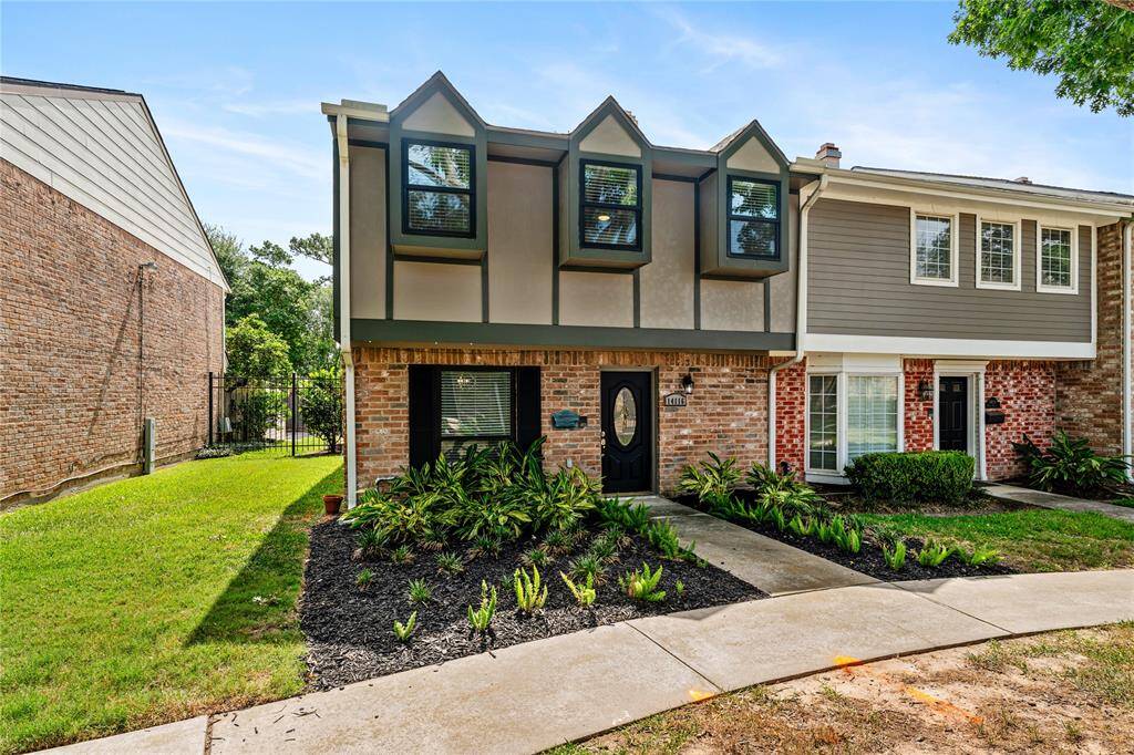 This charming two-story townhouse features a unique facade with large, modern windows and a tidy, landscaped front yard. A mix of brick and siding adds character, while the front pathway leads to a welcoming entrance.