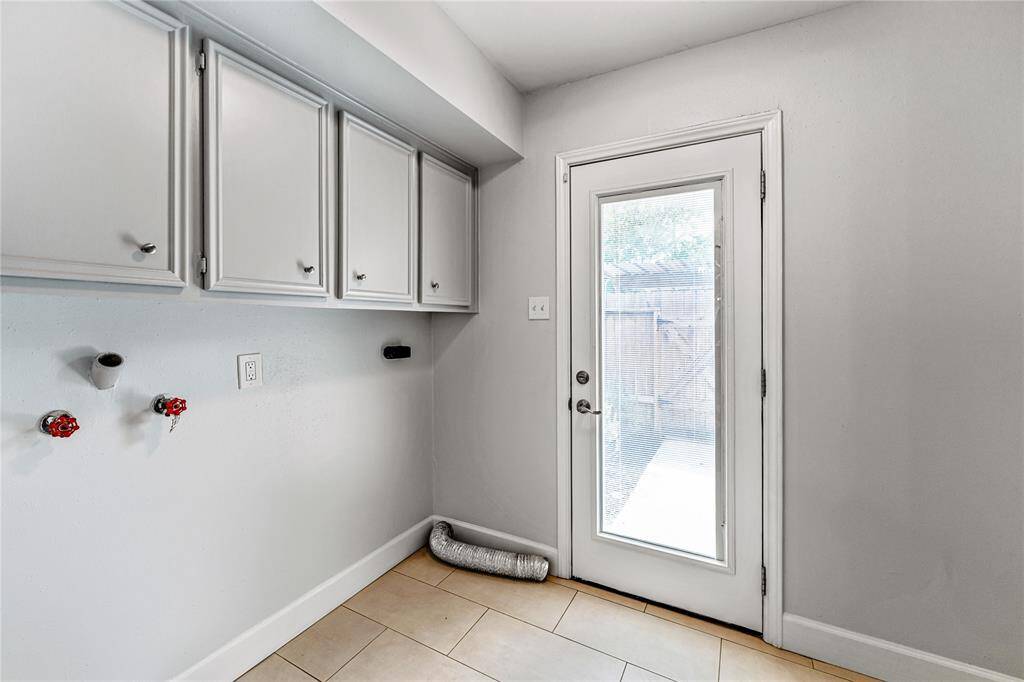 The laundry room features overhead cabinets for storage. A glass door  with built in blinds provides natural light and access to the outdoors.
