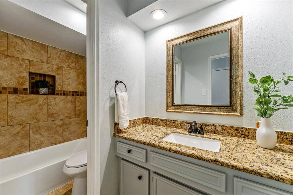 The secondary bathroom follows the main bathroom's aesthetic, featuring a granite countertop, framed mirror, and stylish fixtures. The shower area is tiled with a built-in niche and decorative border, adding a touch of elegance.