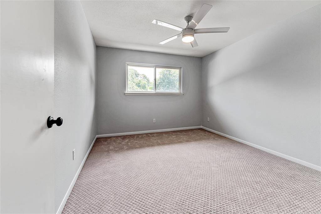 Secondary bedroom featuring neutral walls, a ceiling fan, and a large window providing natural light. The carpeted floor adds warmth, making it a cozy space.