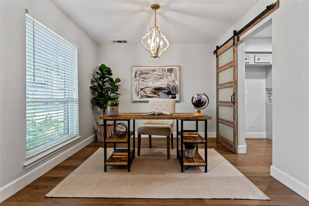 The flex space at the front of the home, with a large window bringing lots of natural light, is presented as a stylish home office. The space, enhanced by the modern chandelier and barn door has a clean, minimalist design and neutral colors.