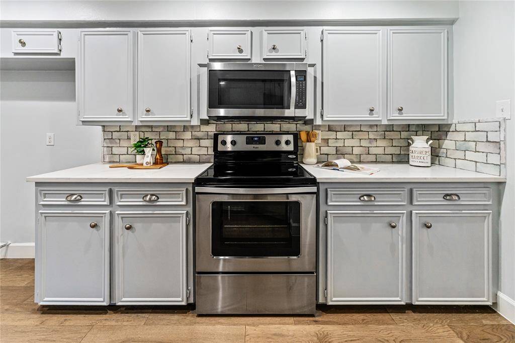The kitchen features stainless steel appliances and soft gray cabinets set against a stylish tile backsplash. The wooden floor adds warmth to the space.