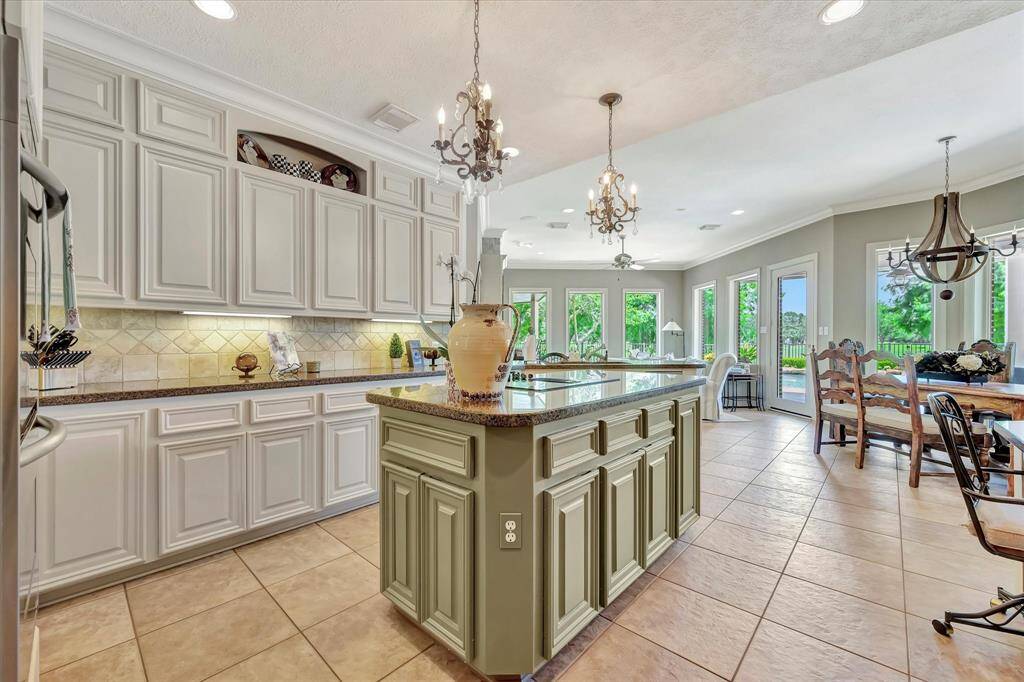 This photo showcases a spacious, elegant kitchen with granite countertops, light cabinetry, and stainless steel appliances. A central island offers additional workspace and seating, while a built-in desk nook adds functionality. A chandelier adds a touch of sophistication, and ample storage includes wine racks and decorative shelving.