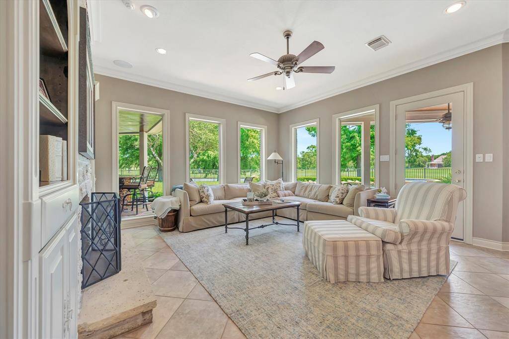 Bright and inviting family room featuring large windows with garden views, neutral tones, and a cozy seating area.  The room is accented with a ceiling fan and opens to an outdoor patio space.