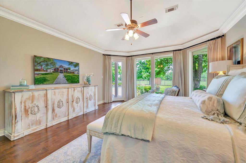 This serene bedroom features hardwood floors, a ceiling fan, and large windows offering a view of lush greenery. Access to outdoors.