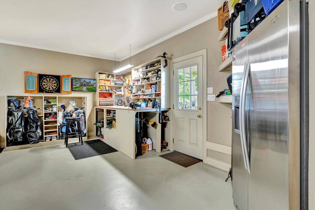 This photo showcases a well-organized garage with ample storage, featuring custom cabinets, shelves for various items, and space for tools and sports equipment. Two doors leading into the home and outdoor kitchen.