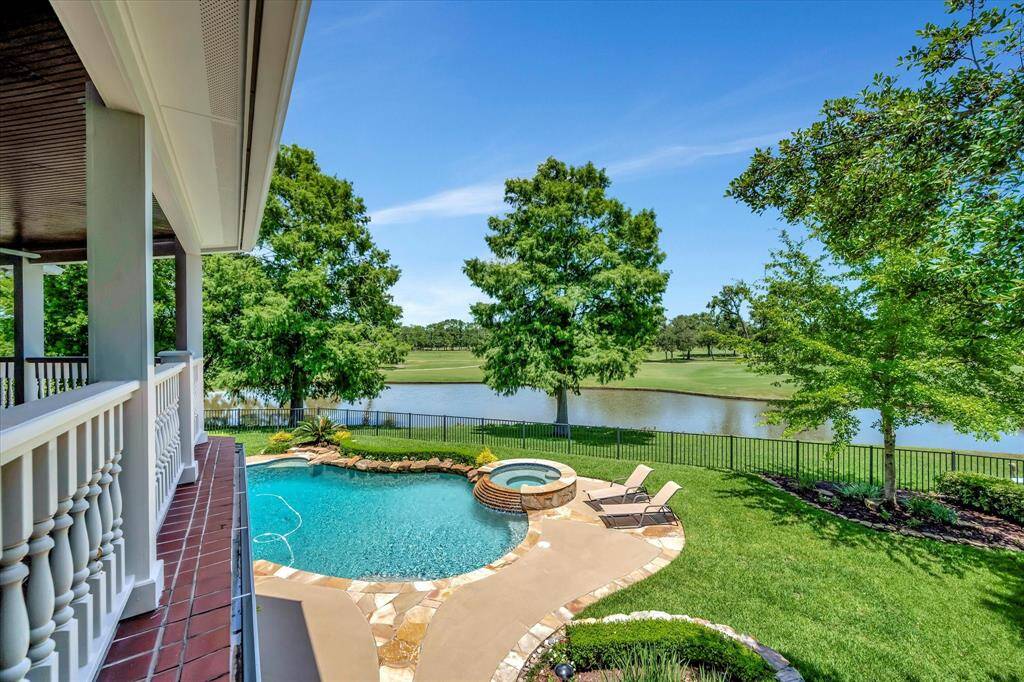 This aerial photo showcases a beautifully landscaped backyard featuring a freeform pool with a connected spa, surrounded by a stone patio. The lush green lawn and tidy landscaping create a serene and inviting outdoor space, perfect for relaxation , privacy and making memories.