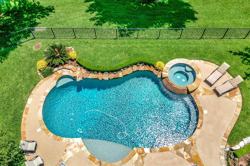 The photo showcases a serene backyard with a sparkling pool and hot tub, surrounded by lush greenery. It overlooks a tranquil pond and open green space, offering a peaceful and private outdoor retreat.