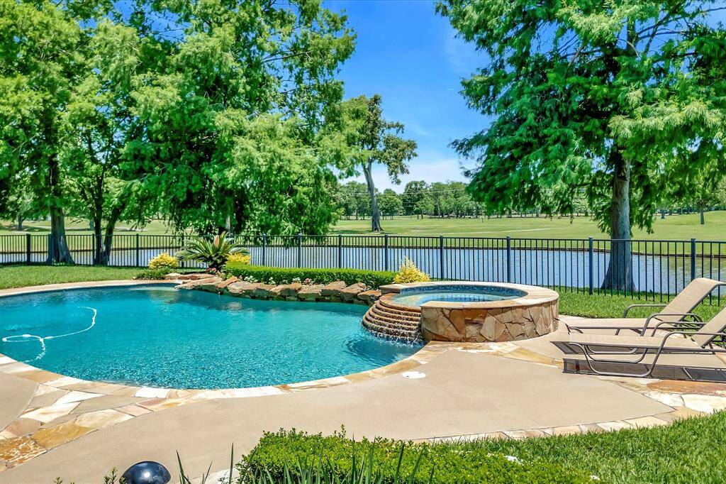 This photo showcases a serene backyard with a beautifully landscaped pool area. The pool has a stone border, surrounded by lush greenery and comfortable seating. A fence provides privacy, and the area is perfect for relaxation and outdoor enjoyment.