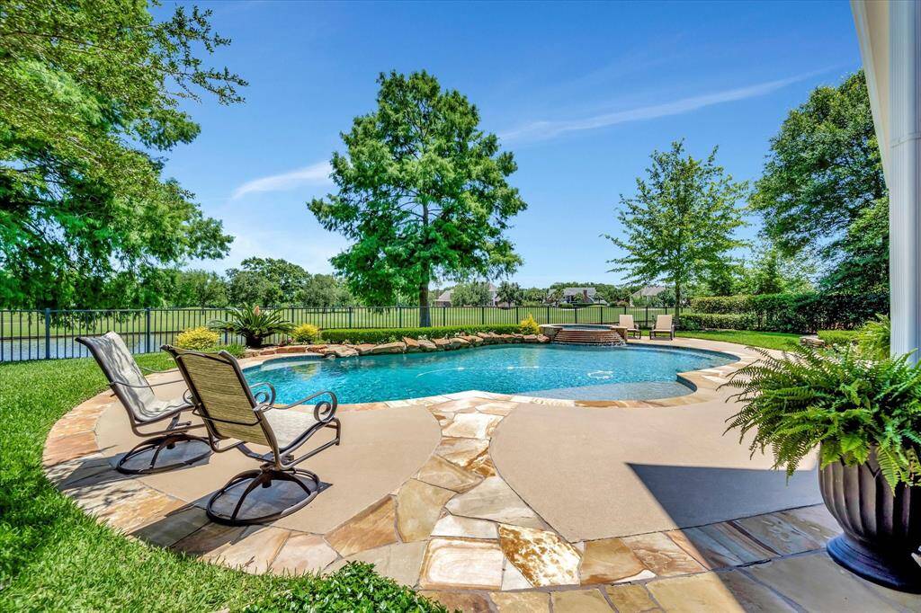 This photo showcases a spacious, covered patio with elegant brickwork, comfortable seating, and a ceiling fan. Surrounded by greenery and afternoon shade and breezes.