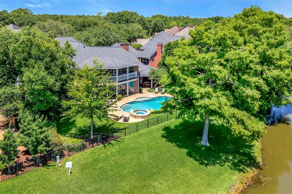 This photo showcases a beautiful backyard with a pool and spa, surrounded by a stone patio. It features lush greenery, a manicured lawn, and a clear view of golf course and pond. Morning sun provides great afternoon weather.