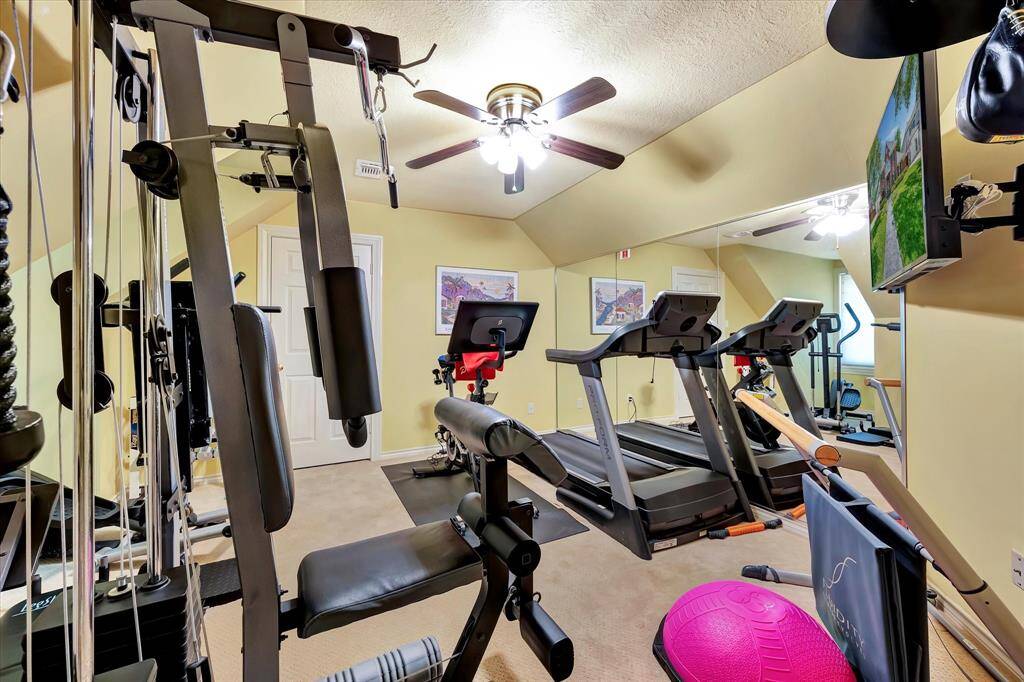 5th bedroom currently used as home gym.  The room is spacious with a ceiling fan, wall-mounted TV, and large mirrors, providing a bright and motivating workout environment.