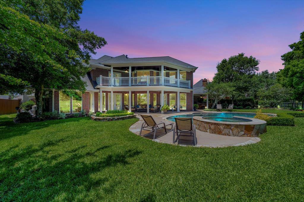 This photo showcases a glimpse of the lovely nature provided by this location a beautifully landscaped backyard with a sparkling pool, natural stone accents, and lush greenery. It features a serene view of a lake and open green space beyond a wrought-iron fence, offering a tranquil and picturesque setting.