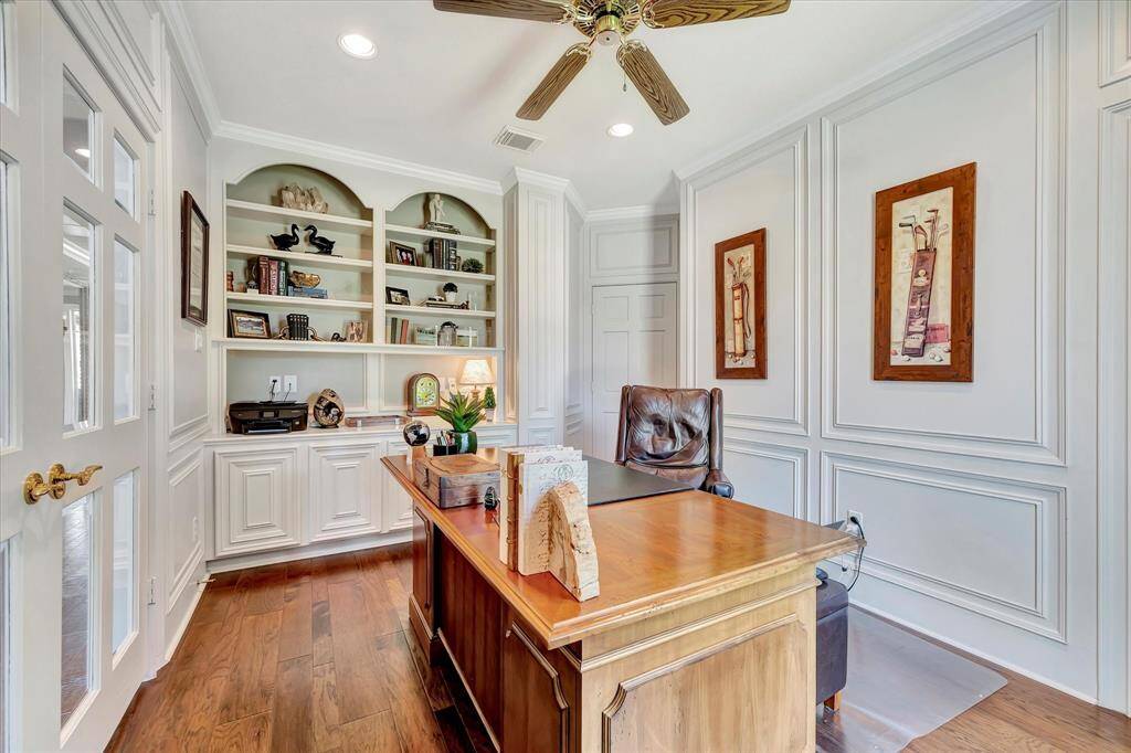 This home office features elegant wood paneling, built-in shelves, and a ceiling fan. It provides a spacious desk area with ample natural light, creating a comfortable and sophisticated workspace. French doors for privacy.