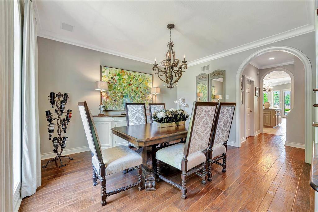 This elegant dining room features hardwood floors, and a classic chandelier.  It opens into a bright kitchen through an arched butlers pantry enhancing the home's open feel. Natural light pours in through large windows, highlighting the tasteful decor and artwork.