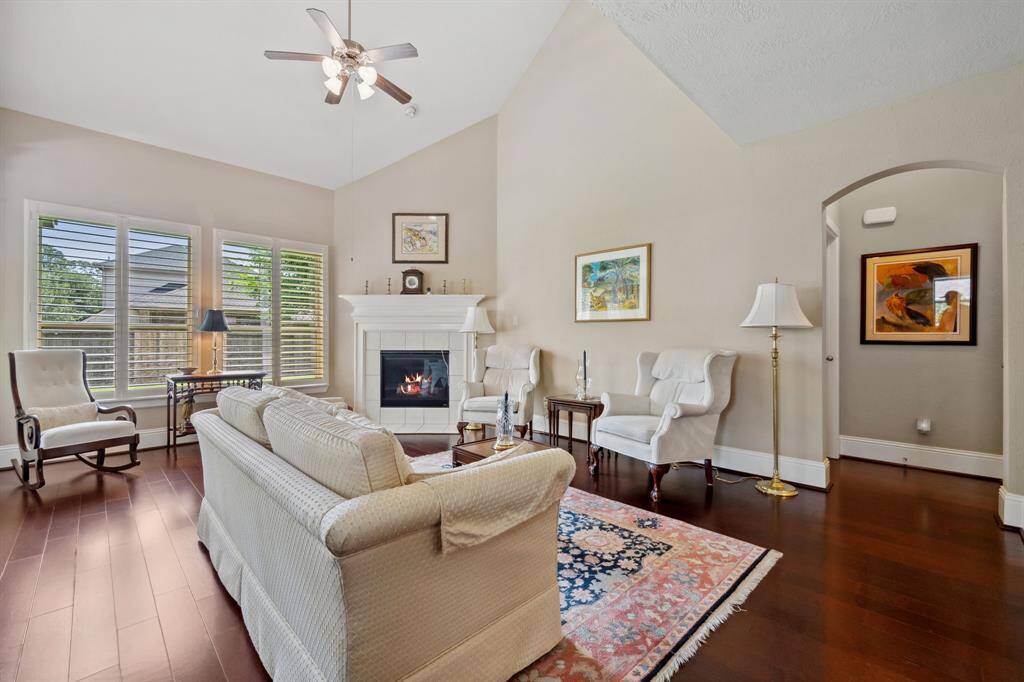 Bright and inviting living room with high ceilings, hardwood floors, and a cozy fireplace. Large windows with plantation shutters provide ample natural light.