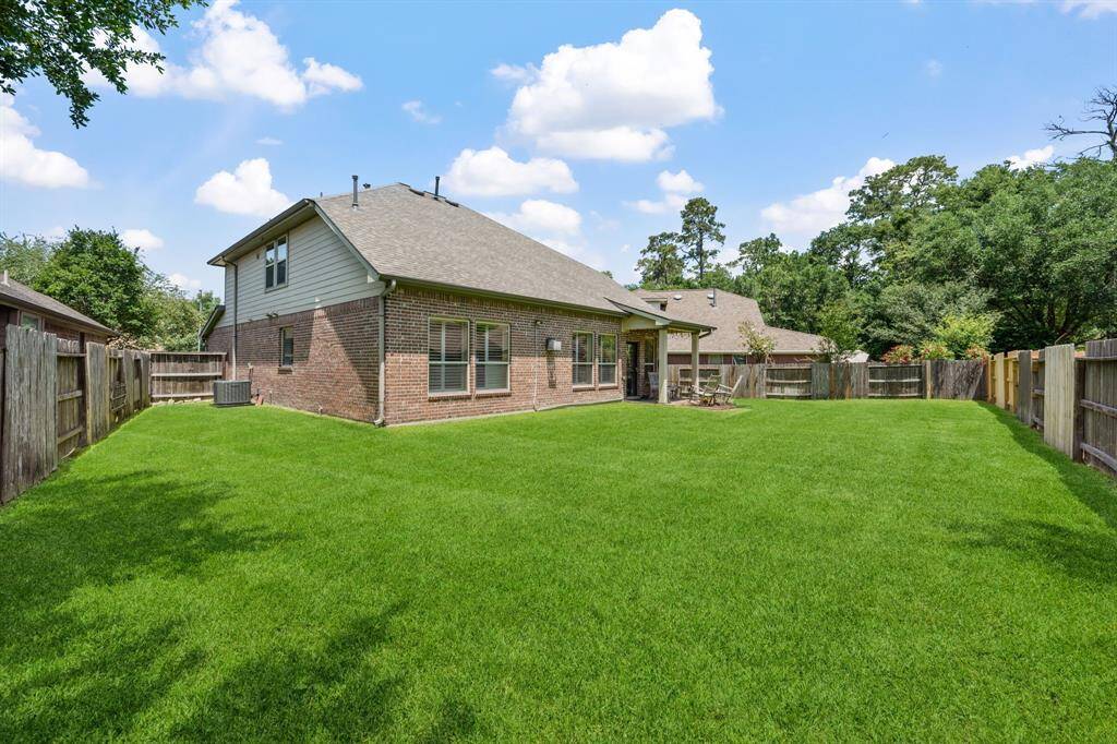 A spacious backyard with well-maintained grass, a brick exterior, and a covered patio. The area is fenced, providing privacy, and is ideal for outdoor activities.