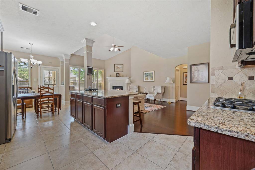 This inviting open-concept space features a modern kitchen with granite countertops and a central island, seamlessly flowing into a cozy living area with a fireplace. The dining area is well-lit with natural light from large windows, and the tiled and hardwood flooring adds a stylish touch.