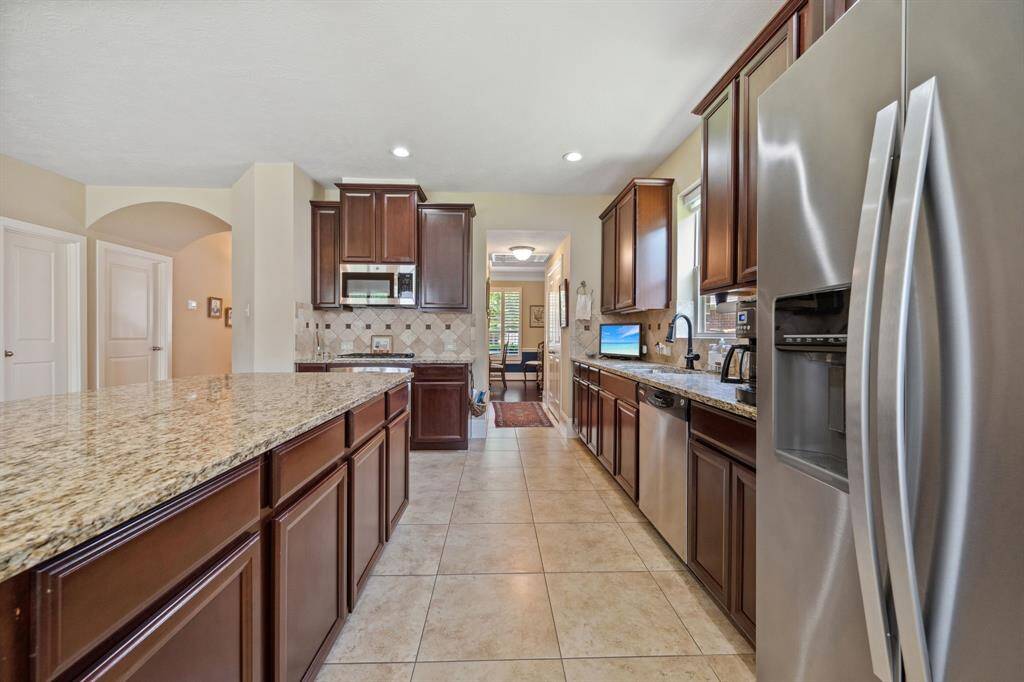 This kitchen features granite countertops, stainless steel appliances, and dark wood cabinetry. The open layout includes a spacious island and tile flooring, creating a modern and functional space.