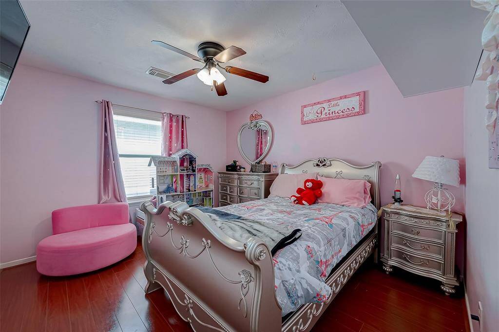 This cozy bedroom is designed with a playful, princess theme, featuring pink walls and elegant furniture. It has a comfortable bed, a cute seating area, and ample natural light from the window, creating a charming space for a child.
