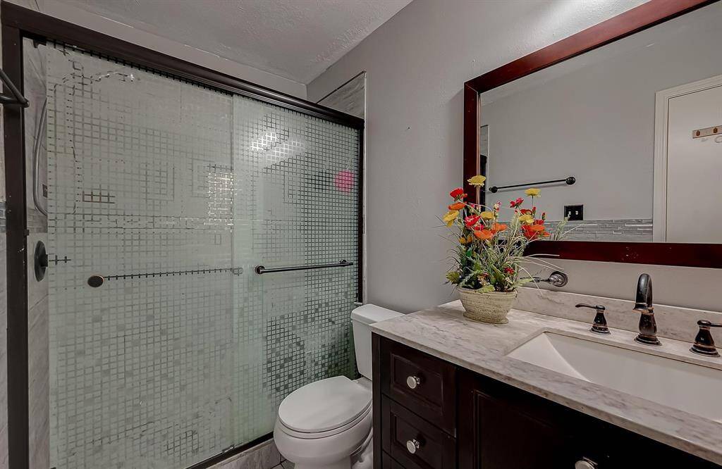 This bathroom features a modern glass-enclosed shower with a geometric pattern, a dark wood vanity with a marble countertop, and a large mirror. It is accented by a floral arrangement, adding a touch of color and elegance.