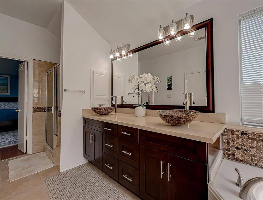 This bathroom features a modern design with a double vanity, vessel sinks, and a large mirror. It has a spacious shower, elegant lighting, and neutral tones, creating a clean and inviting atmosphere.