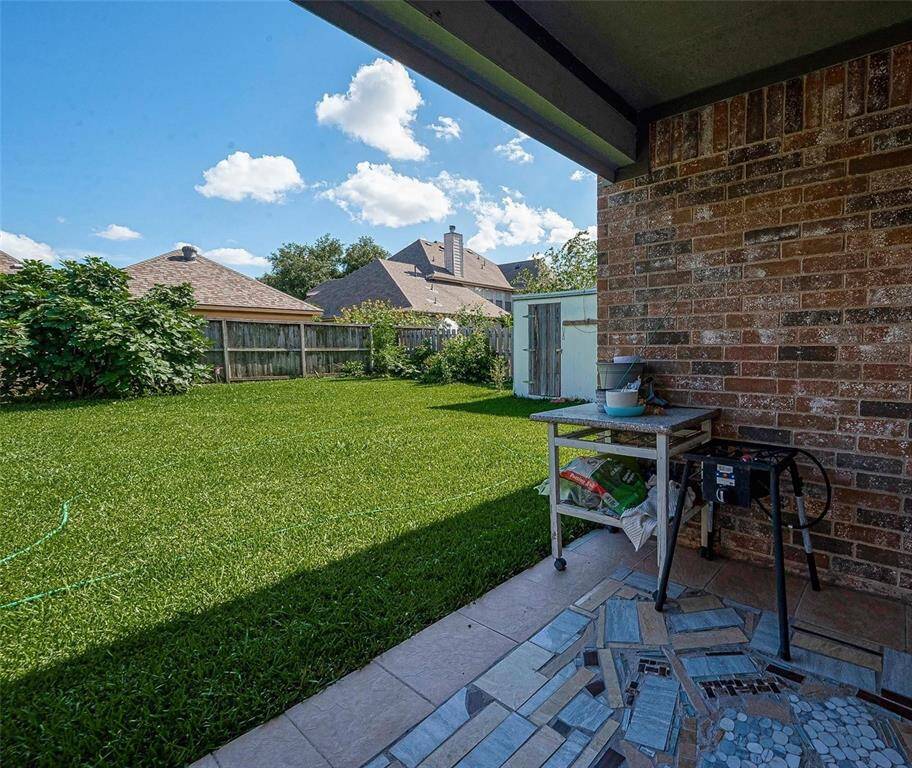 This photo showcases a spacious backyard with a well-maintained lawn and a covered patio area. It features brick siding, a small utility table, and is enclosed by a wooden fence, providing privacy and a cozy outdoor space.