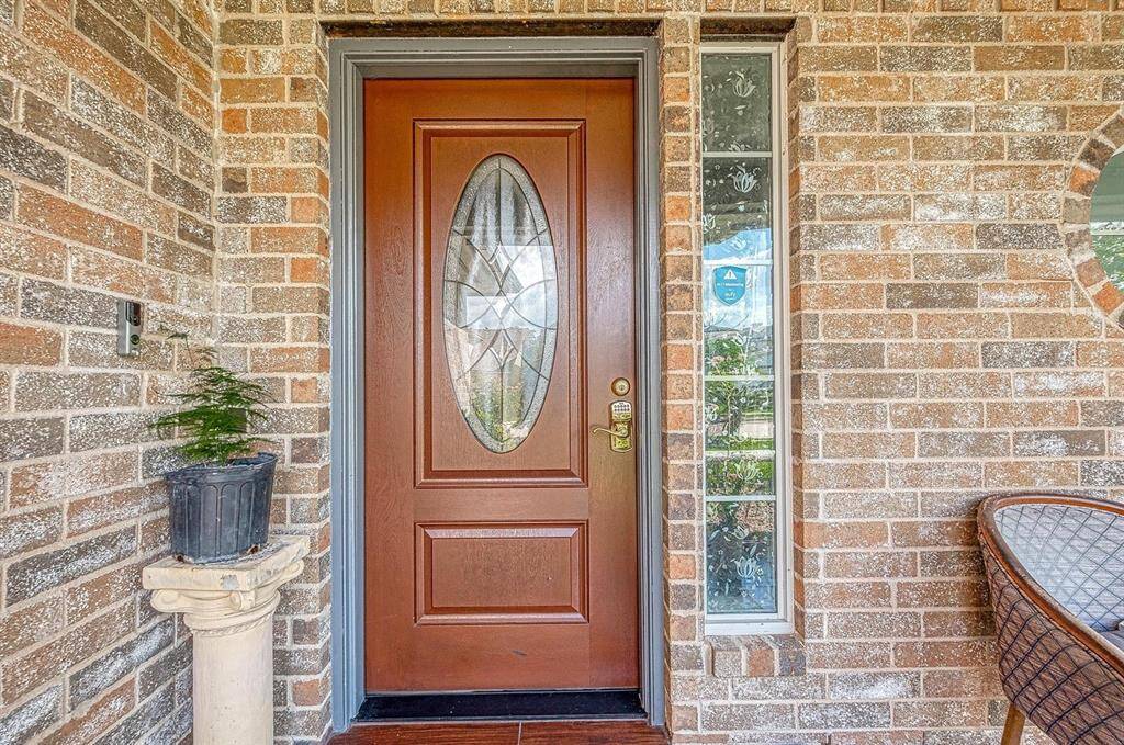 This inviting entryway features a rich wooden door with elegant glass detailing, framed by a warm brick exterior. A small potted plant adds a touch of greenery.