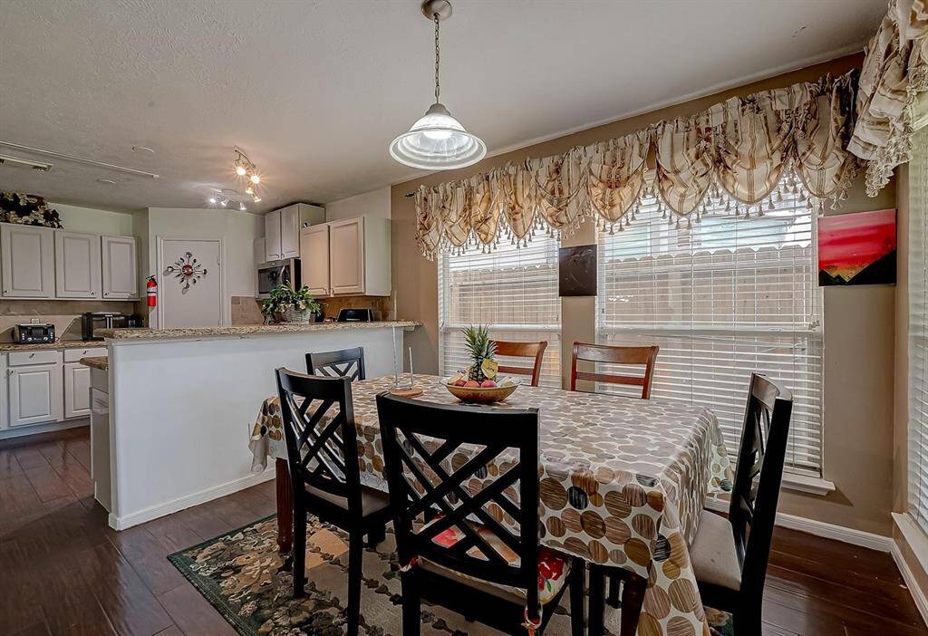 This photo shows a cozy dining area adjacent to a kitchen with white cabinetry and granite countertops. Large windows with elegant drapes provide natural light, creating a warm and inviting atmosphere.