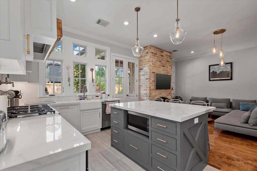 This home boasts an open-concept kitchen and living area. The kitchen features a large island with a marble countertop and pendant lighting, while the living space includes a cozy seating area and a brick accent wall. Natural light streams through multiple windows, enhancing the bright and inviting atmosphere.
