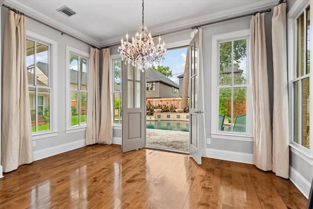 This room features elegant hardwood floors, large windows with curtains, and a striking chandelier. French doors open to a backyard with a pool, offering a bright and inviting atmosphere.