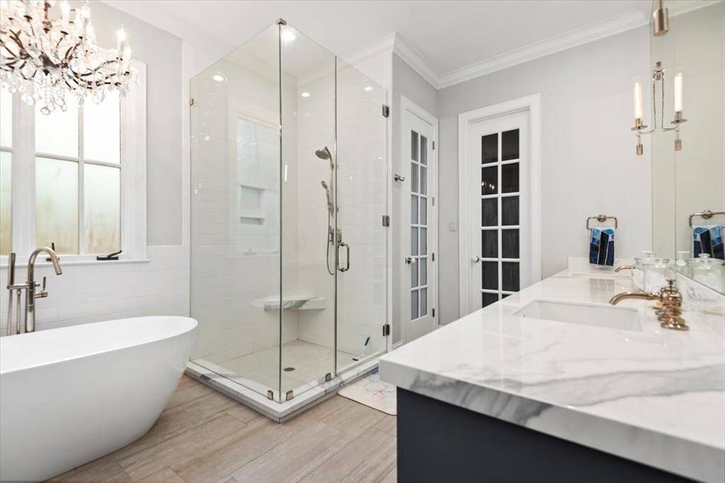 The elegant en suite bathroom features a freestanding tub, a spacious glass-enclosed shower, and dual sinks with marble countertops. The soft lighting and modern fixtures create a luxurious, spa-like atmosphere.