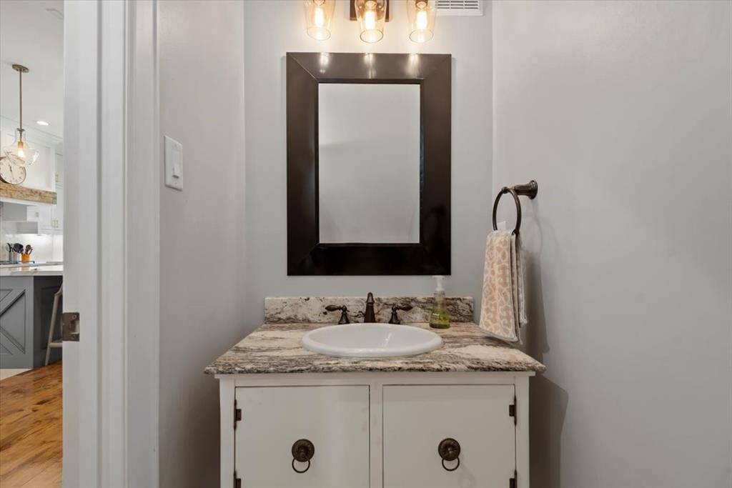 This photo features a modern bathroom with a granite countertop vanity, a round sink, and a sleek black-framed mirror.