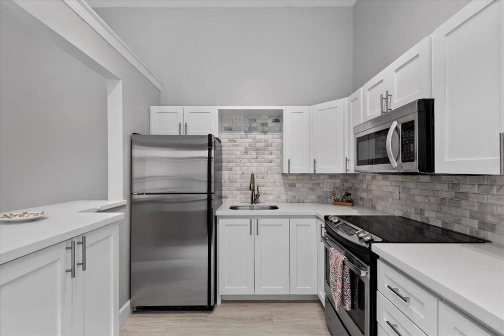 This modern kitchen features sleek white cabinetry, stainless steel appliances, and a stylish gray tile backsplash, creating a clean and contemporary look.
