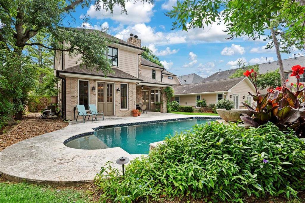 This inviting backyard features a charming two-story home with a beautiful pool surrounded by lush landscaping. The spacious patio offers an outdoor fireplace and a serene atmosphere perfect for relaxation or entertaining.