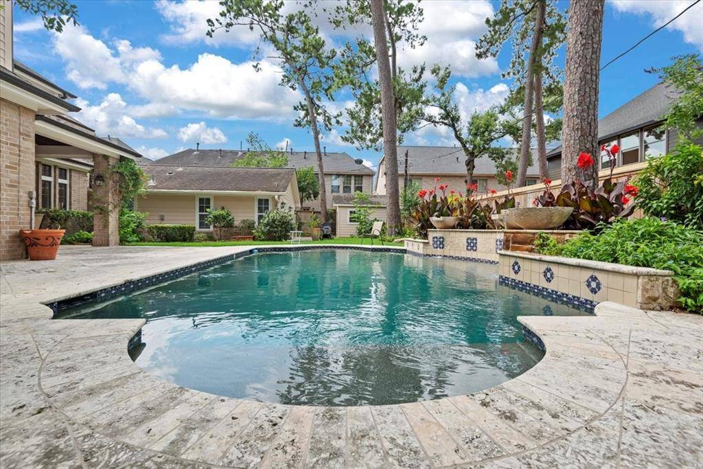 This inviting backyard features a beautifully designed gunite pool with travertine decking surrounded by lush greenery and elegant landscaping. The spacious patio offers ample room for outdoor relaxation and entertainment, creating a serene oasis perfect for enjoying sunny days.