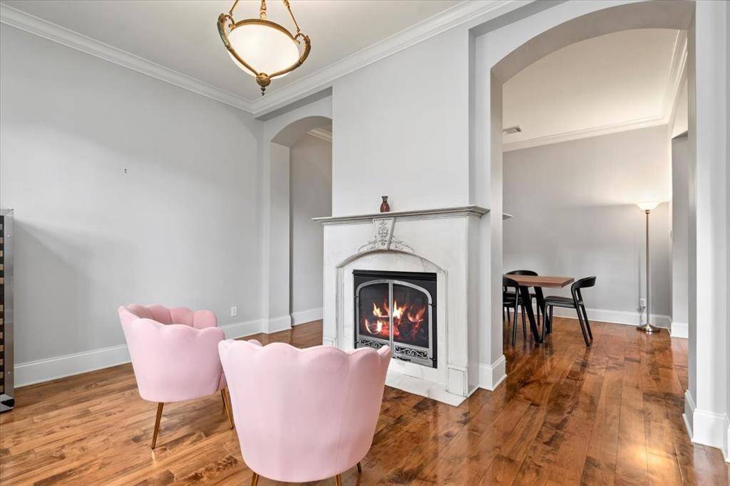 This inviting living space features a cozy double sided fireplace and tall ceilings. The room opens to a dining area through an arched entryway, creating a seamless flow. The neutral walls and modern lighting enhance the room's warmth and charm.