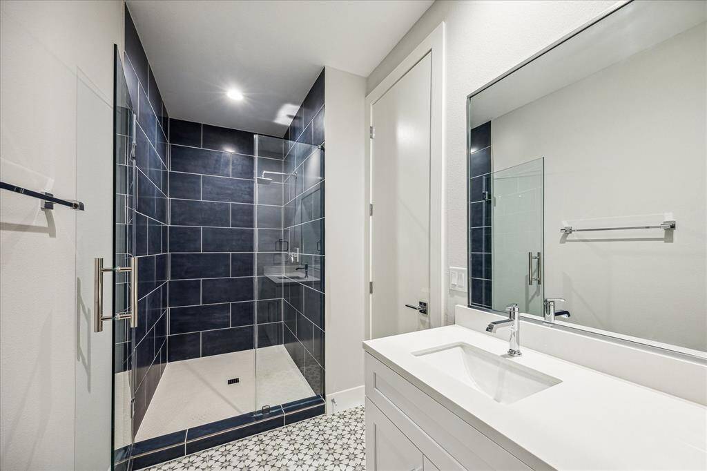 The luxurious bathroom features a contemporary dark-tiled shower with a glass door, providing a spalike experience at home. The bold design and high-end finishes make this bathroom a standout.