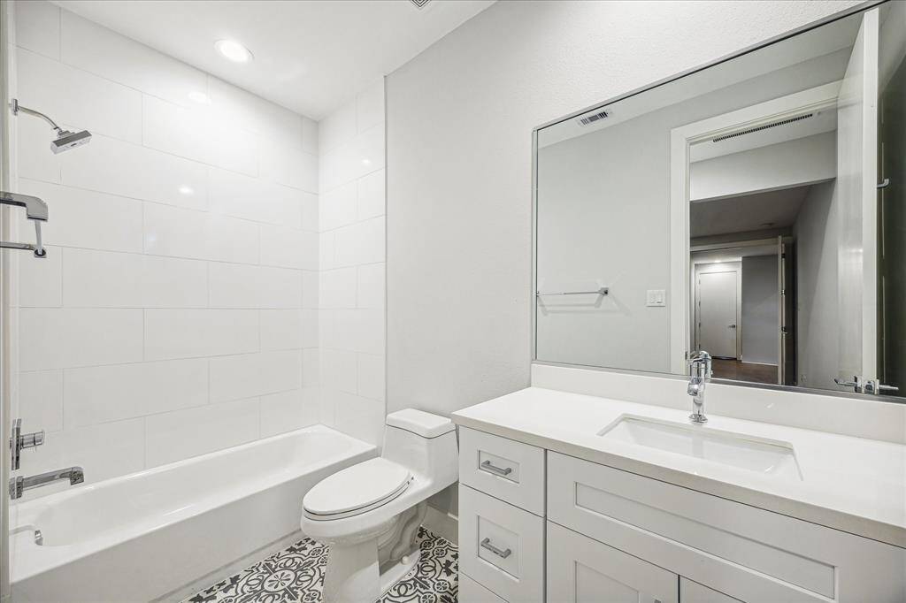 Elegant guest bathroom with clean, white tiles and stylish patterned flooring. This space blends functionality with a contemporary aesthetic, offering ample storage and a clean, refreshing look ideal for guests.