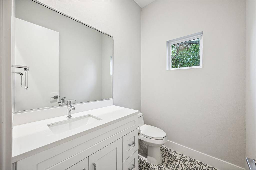 This bathroom is a blend of style and practicality, featuring a minimalist vanity, polished fixtures, and a large mirror that enhances the space. The charming patterned floor adds a touch of character, making it a perfect spot for guests.