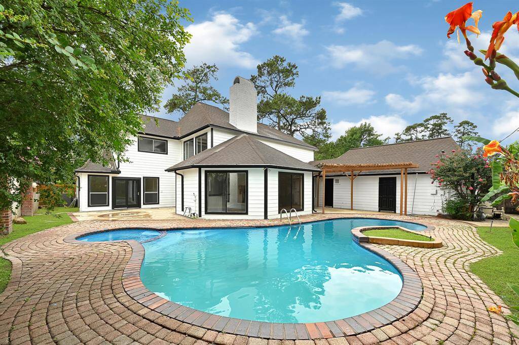 Resort-style backyard with curved pool, patio seating areas, and garden-lined fencing.