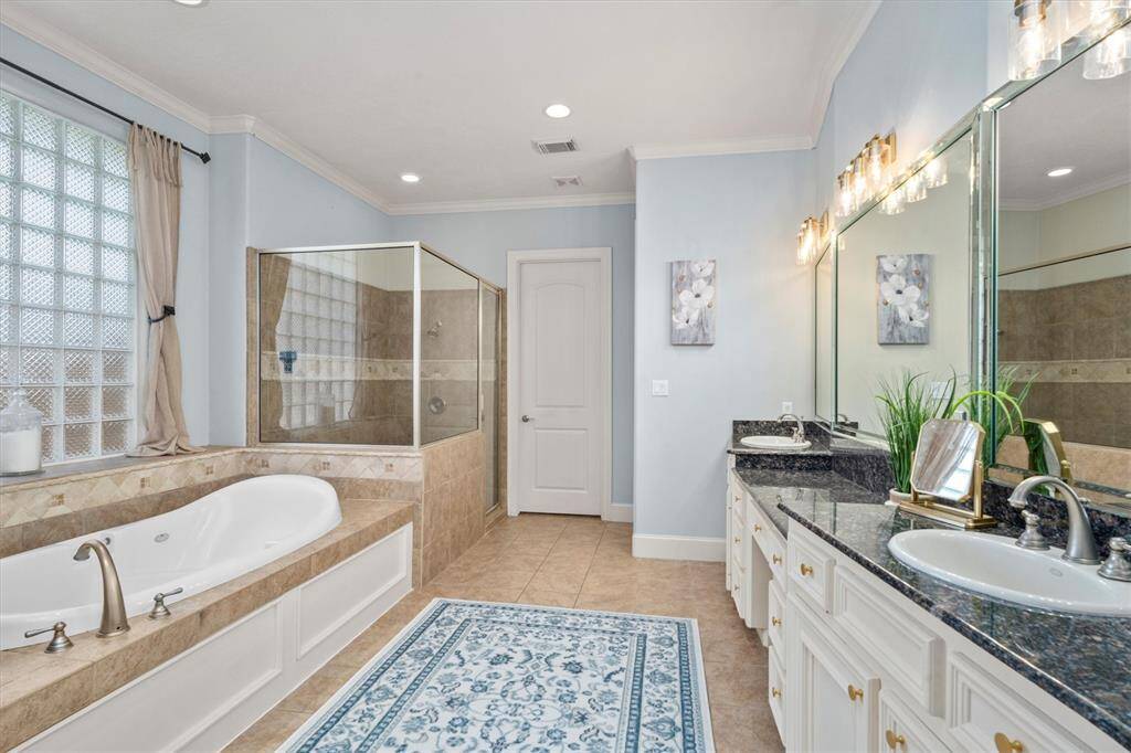 Executive bath with double sinks, sit space for vanity, and oversized jetted tub and shower