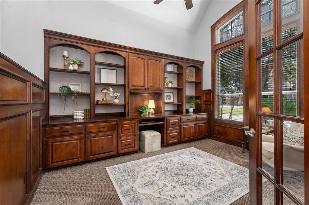 8” glass French doors open to cathedral ceiling home office with custom built-ins, updated wallpaper accent, and freshly painted
